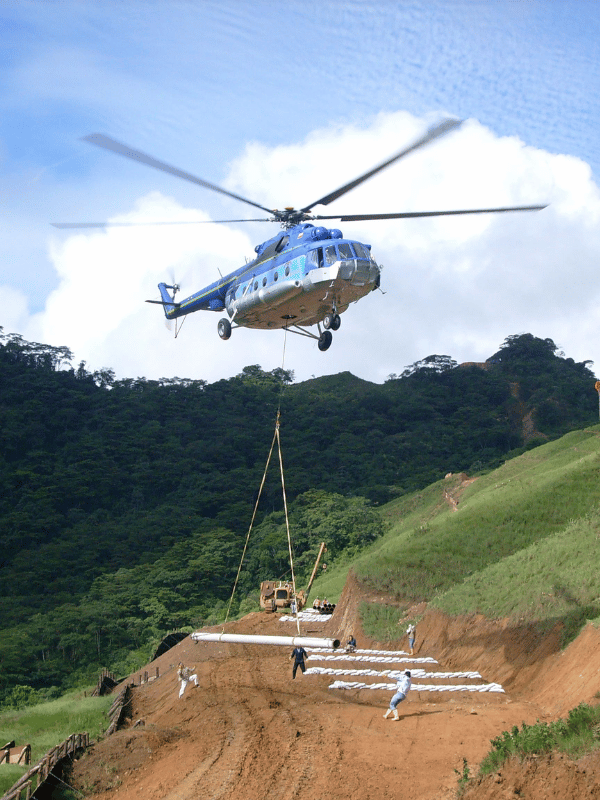 Helicopter airlifting pipe sections to a mountain work front