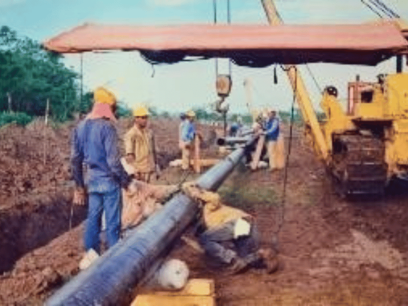 Crew lowering pipe into the trench with machinery support